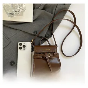 Mini brown crossbody bag with decorative buckle and phone for scale comparison