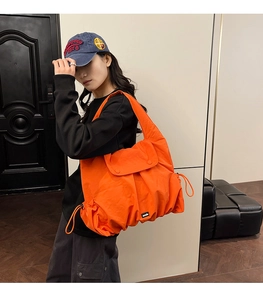 Detail of orange drawstring nylon tote bag featuring adjustable sides and top flap cover