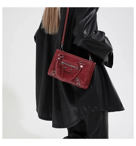 Detail of burgundy motorcycle bag with studs, adjustable strap and pebbled leather texture