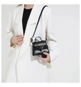 Close-up of a minimalist black leather mini crossbody bag styled on a white blazer outfit