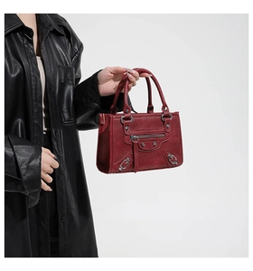Detail of burgundy wine rivet handbag with pebbled texture and long tassel zipper pulls