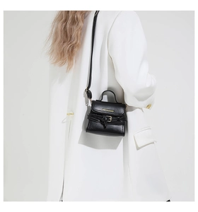 Détail d'un mini sac bandoulière en cuir noir avec lettres dorées et boucle sur un costume blanc