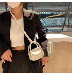 Detail of a creamy white semi-circular mini handbag with a unique integrated round handle