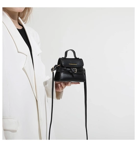 Détail du mini sac bandoulière noir avec lettrage doré et texture cuir sur costume blanc