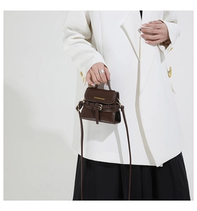 Détail d'un mini sac à main en cuir marron foncé avec boucle et poignée porté par un modèle