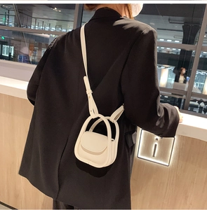 Detail of a creamy white mini leather crossbody bag with double handles and a round flap
