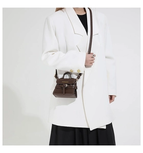 Détail d'un mini sac bandoulière marron foncé avec sangle décorative sur un blazer blanc