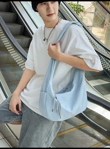 Detail der hellblauen Nylon-Hobo-Tasche mit Kordelzug, getragen auf einer Rolltreppe