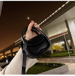 Close-up of a black mini leather handbag featuring a half-moon shape and detachable strap