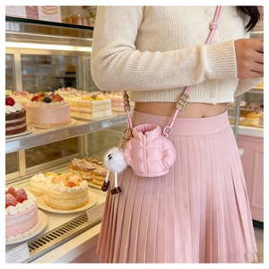 Pink puffer mini crossbody bag detail with white plush charm and woven shoulder strap
