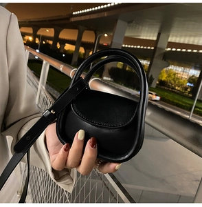 Detail of a mini black leather handbag with round handles and gold metal hardware
