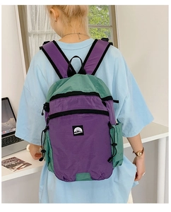 Detail eines lila-grünen Nylon-Rucksacks mit Berg-Logo, getragen von einem weiblichen Model