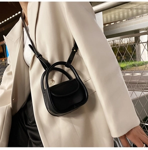 Close-up of black matte leather mini bag with circular handle on model in city setting