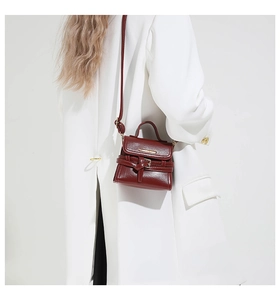 Détail d'un mini sac à main bordeaux avec décoration ceinture porté par un mannequin en veste