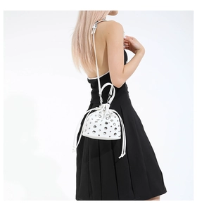 White mini bucket bag with silver studs and drawstring, worn by model over shoulder