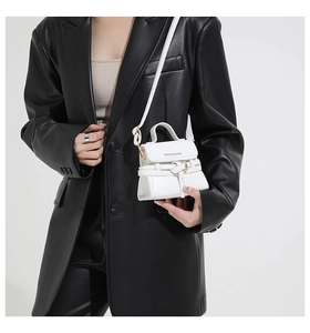 Detail of white mini leather handbag with decorative straps and gold lettering on white