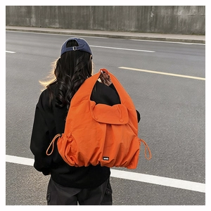 Outdoor view of a large orange nylon shoulder bag with drawstring and flap closure