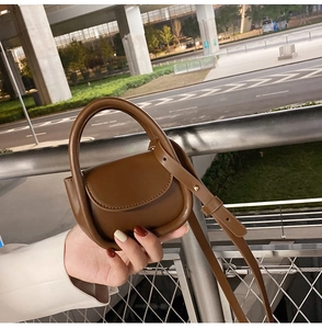 Macro detail of brown leather mini crossbody bag featuring neat stitching and metal buckle