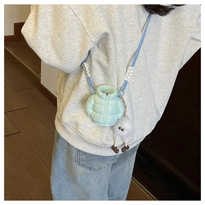 Detail of mint green quilted puffer crossbody bag with blue strap and plush charm
