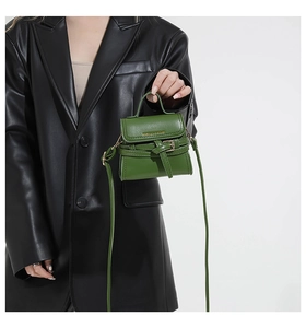 Détail d'un mini sac bandoulière vert forêt avec boucle décorative tenu par un mannequin
