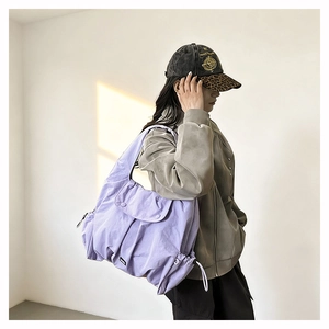 Detail of lavender purple nylon crossbody bag showing the drawstring side and front flap pocket