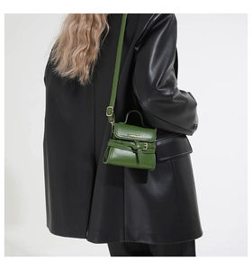 Gros plan d'un mini sac à bandoulière vert en cuir sur veste noire avec détail de boucle