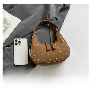 Detail of brown suede crescent bag with silver stud rivets on gray fabric background