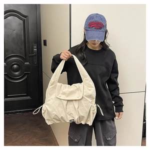 Close-up of large beige nylon tote bag featuring drawstring sides and flap closure