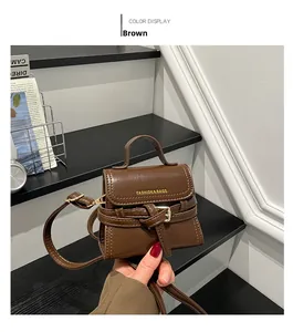 Detail of brown leather handbag with gold lettering and strap buckle on a black step