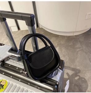 Close-up of black mini handbag with double handles placed on a silver suitcase
