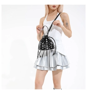 Detail of a black drawstring bucket bag featuring silver rivets and a chain strap