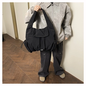 Detail view of black large capacity shoulder bag with drawstring pockets and flap closure