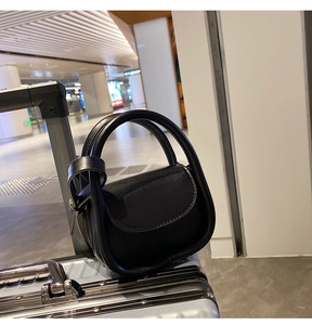 Detail view of a black mini handbag with a curved handle on a metallic suitcase