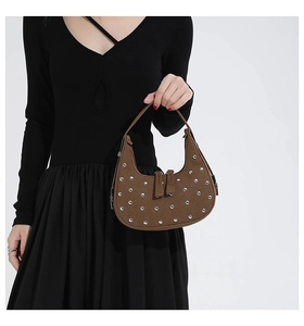 Detailed close-up of brown suede crescent bag featuring silver rivet studs and dual zippers