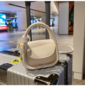 Close-up of cream mini handbag on silver luggage case showing curved handle and PU texture