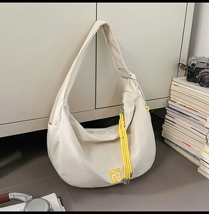 Detailansicht der cremeweißen Halbmond-Umhängetasche mit gelbem Logo und Quaste
