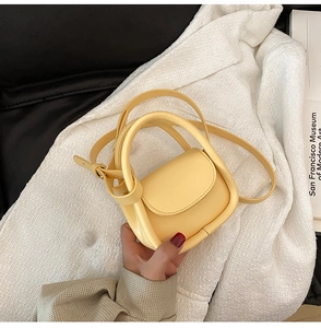 Detail of light yellow mini handbag with smooth faux leather texture and round handle