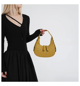Close-up of yellow punk crescent handbag with silver rivets worn by model in black dress