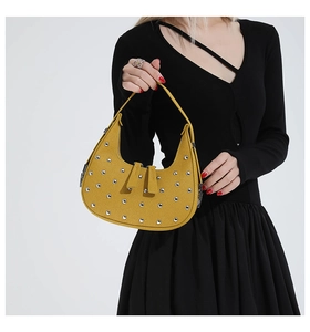 Detail of yellow crescent bag with silver studs carried by a model in a black dress