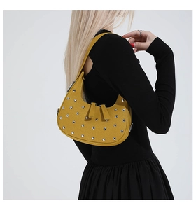 Detail of yellow crescent shoulder bag with silver studs worn by a model in black dress