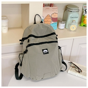 Detail eines hellgrau-grünen Rucksacks mit Karomuster, Ripstop-Stoff und Seitentaschen