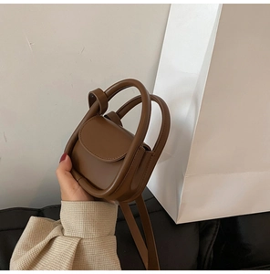 Detail view of brown mini crossbody bag with circular handle and matte leather finish