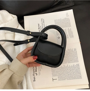 Detailed macro of a black mini leather handbag featuring a thick curved handle and silver hardware