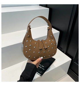 Elegant brown punk style rivet handbag held by hand in a minimalist studio setting.