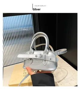 Detail of silver shell-shaped mini bag with glossy finish held by hand to show size