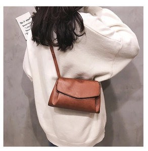 Close-up of a brown vintage leather crossbody bag with wave-edge flap worn by a model