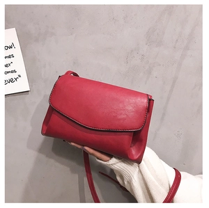 Detail of red leather crossbody bag with flap closure and adjustable shoulder strap