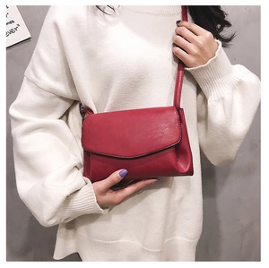 Detail of red faux leather crossbody bag paired with a white knit sweater for a casual style