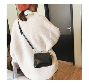 Detail of black glossy frame bag with metallic clasp worn with a beige winter coat