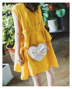 Detail of white heart crossbody bag with large bow on yellow tiered cotton dress